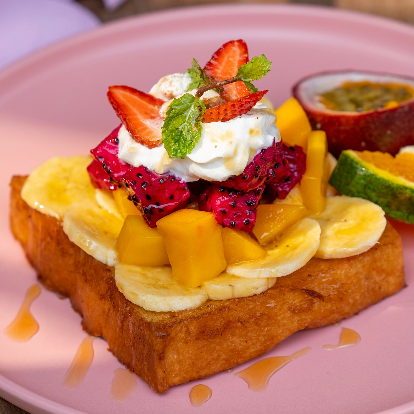 Golden-fried Crispy French Toast, piled high with sun-ripened tropical fruits including sweet mango, sliced banana, and vibrant dragon fruit, topped with velvety whipped cream and honey at YESH! Tribe | Eat & Vibe in Hoi An