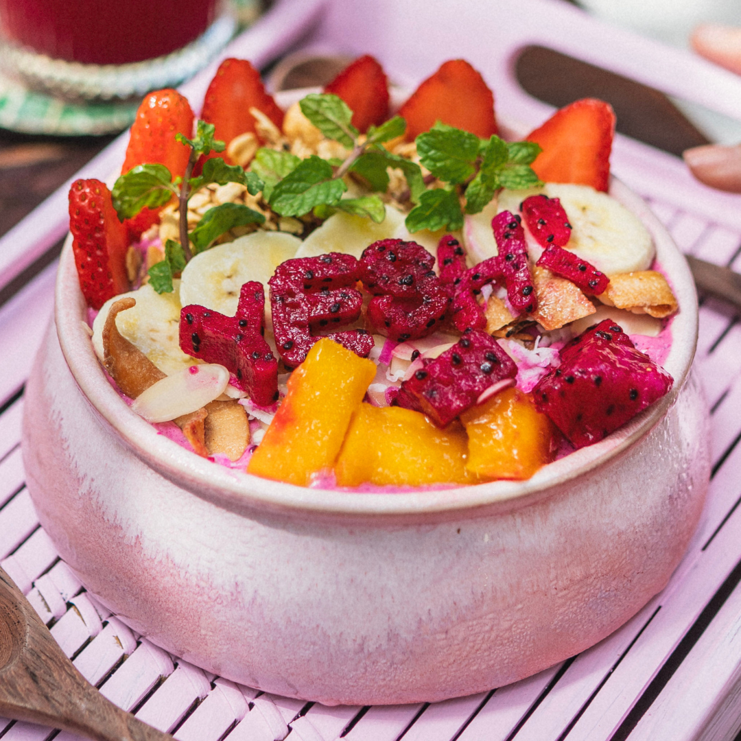 Vibrant Frozen Dragon Bowl blended with local red dragon fruit, mango, banana, and coconut cream, topped with homemade granola, premium nuts, and fresh seasonal fruits arranged to spell YESH! at YESH! Tribe | Eat & Vibe